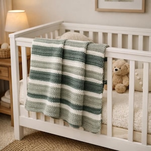 Peut inclure: Une couverture crochetée à la main présentant des rayures horizontales dans des tons alternés de vert sauge, de vert forêt foncé et de blanc crème. Le textile a un aspect tissé et texturé avec des motifs de points cohérents sur toute la pièce.