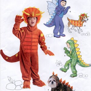 May include: A sewing pattern for making dinosaur costumes for children and a dog. The pattern includes a triceratops, a green dinosaur, a purple dinosaur with wings, and a dog costume with a dinosaur head. The pattern is from Simplicity and the pattern number is 1765.