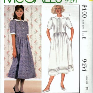 Op de afbeelding: McCall's 9434 Laura Ashley naaipatroon-envelop met twee jurkvariaties. Model B is een blauwe jurk met bloemenprint, witte kraag en manchetten. Model A is een effen witte jurk met een Peter Pan-kraag, korte mouwen en plooien.