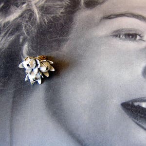 May include: A white metal flower cluster earring with a gold tone accent. The earring is a cluster of small white flowers with a gold tone accent in the center.