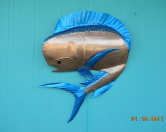 May include: A metal sculpture of a blue and gold mahi-mahi fish mounted on a turquoise wall. The fish is facing left and has a blue dorsal fin and tail.