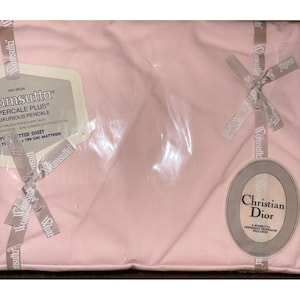 May include: A pink fitted sheet in a plastic package, with a tag that reads "Wamsutta Percale Plus Luxurious Percale". The sheet is for a 190 cm mattress and has a Christian Dior tag.