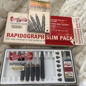 May include: A Koh-I-Noor Rapidograph Slim Pack set, including pens, ink, and accessories. The set features a red and white box with the Rapidograph logo and product information. The set includes a clear plastic tray with various pen components and a bottle of black drawing ink.