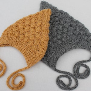Könnte beinhalten: Zwei gestrickte Baby-Mützen mit Bändern. Eine Mütze ist senfgelb und die andere ist grau.