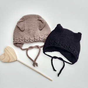 May include: Two knitted baby hats with ear flaps. One hat is brown and the other is black.