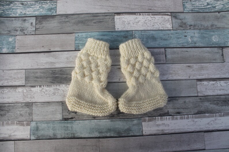 May include: A pair of cream-colored knitted baby booties with a textured pattern.