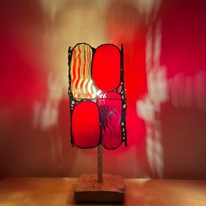 May include: A red and yellow stained glass lamp with a wooden base. The lamp is lit and casting a warm glow.