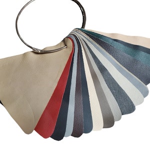 May include: A fan-shaped leather swatch book with a metal ring. The swatches are in various shades of gray, beige, brown, red, and blue.