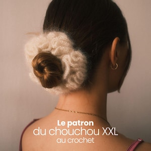 May include: A woman's hair is styled in a bun, adorned with a large, fluffy, cream-colored crocheted scrunchie. The image includes text in French: "Le patron du chouchou XXL au crochet" and "Par Emsau".