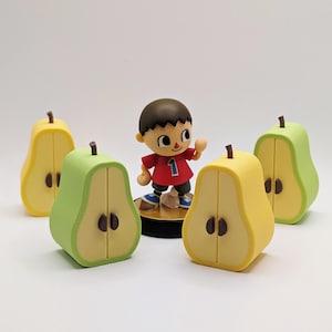 Puede incluir: Una figura de un personaje del videojuego Animal Crossing, con una camisa roja con el n&uacute;mero 1. Cuatro recipientes en forma de pera en amarillo y verde rodean la figura. Las peras tienen semillas y tallos marrones.