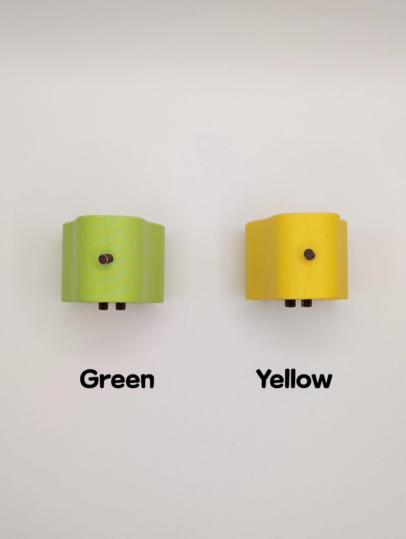 Puede incluir: Dos apliques de pared, uno verde y otro amarillo, est&aacute;n montados en una pared blanca. Cada aplique tiene una parte superior e inferior curvadas, con un bot&oacute;n marr&oacute;n oscuro y dos peque&ntilde;as clavijas negras. Las palabras "Verde" y "Amarillo" est&aacute;n escritas debajo.