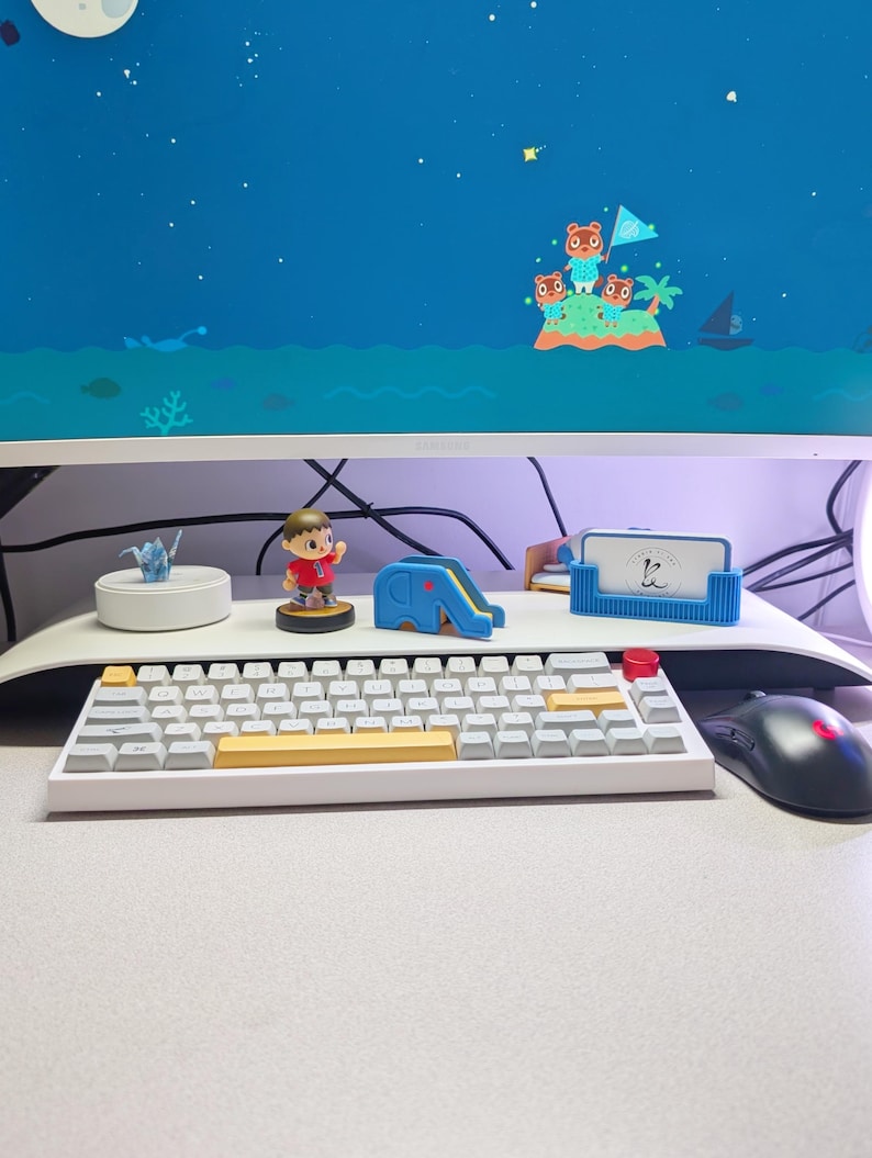 May include: A white mechanical keyboard with yellow and red keycaps sits on a desk. A computer monitor displays a cartoon scene of an island with characters. A mouse and various desk accessories are also visible.