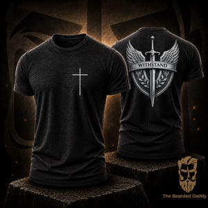 May include: Dark grey t-shirt with a white cross on the front. The back of the shirt features a shield design with a sword, wings, and the word "WITHSTAND". The shirt is displayed on a dark brown surface.
