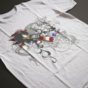 Könnte beinhalten: Weißes T-Shirt mit einer Grafik von Shadow the Hedgehog aus der Videospielserie Sonic the Hedgehog. Das Design zeigt die Figur in Aktion mit roten, schwarzen und gelben Akzenten sowie dem Sonic-Logo.