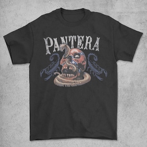 May include: Black t-shirt featuring the band name "PANTERA" in distressed white lettering. The graphic includes a skull with a snake and two scorpions in blue and tan colors.