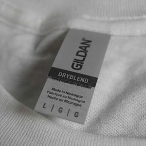 Puede incluir: Primer plano de una camiseta blanca con una etiqueta gris Gildan. La etiqueta dice "DRYBLEND" y "Hecho en Nicaragua". La etiqueta tambi&eacute;n muestra la talla "L G G".