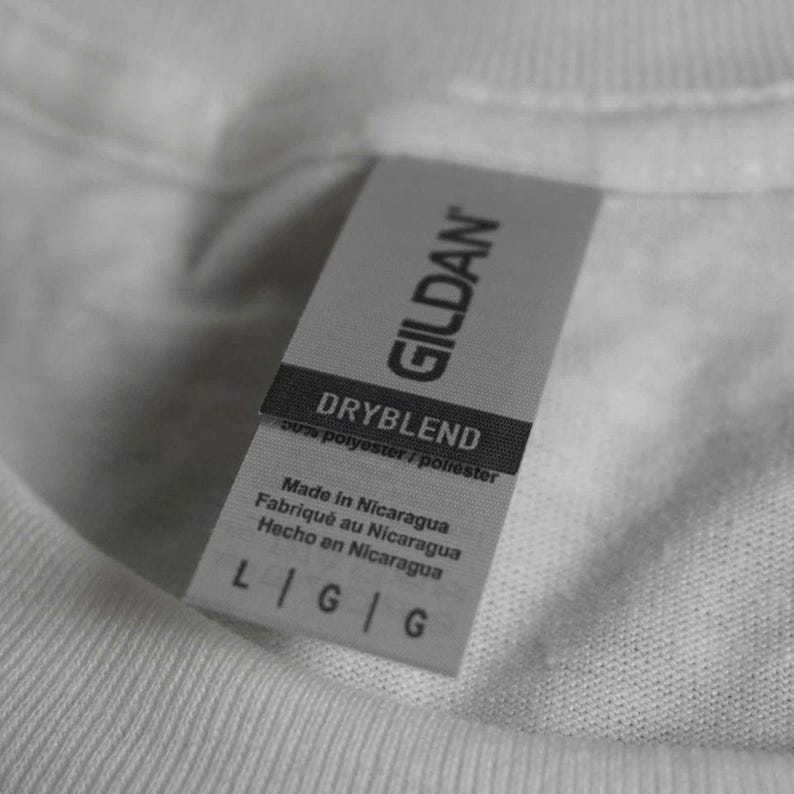 Puede incluir: Primer plano de una camiseta blanca con una etiqueta gris Gildan. La etiqueta dice "DRYBLEND" y "Hecho en Nicaragua". La etiqueta tambi&eacute;n muestra la talla "L G G".
