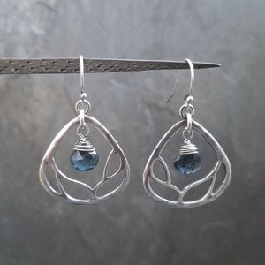 May include: Silver dangle earrings with a delicate leaf design and a dark blue gemstone drop.
