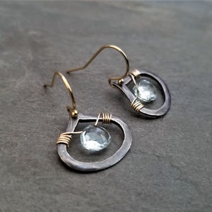 May include: A pair of silver teardrop earrings with gold accents and a clear gemstone in the center of each teardrop.
