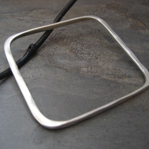 May include: A silver square bangle bracelet with a hammered finish.