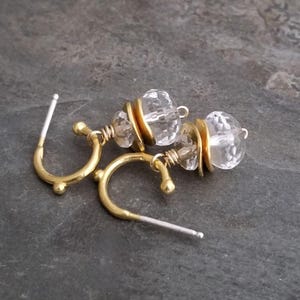 May include: A pair of gold hoop earrings with clear faceted crystal beads. The earrings have a simple design and are perfect for everyday wear.