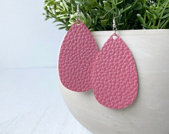 May include: A pair of pink teardrop-shaped earrings with a textured leather finish. The earrings have silver hooks.