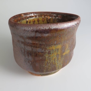 May include: A small, brown ceramic bowl with a speckled glaze. The bowl has a rounded shape and a slightly flared rim.