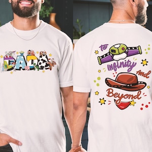 Puede incluir: Camiseta blanca con la palabra "DADA" en letras de colores, con personajes de dibujos animados y estrellas. La parte trasera de la camiseta tiene la frase "To Infinity And Beyond" con un dise&ntilde;o de guardabosques espacial y un sombrero de vaquero.