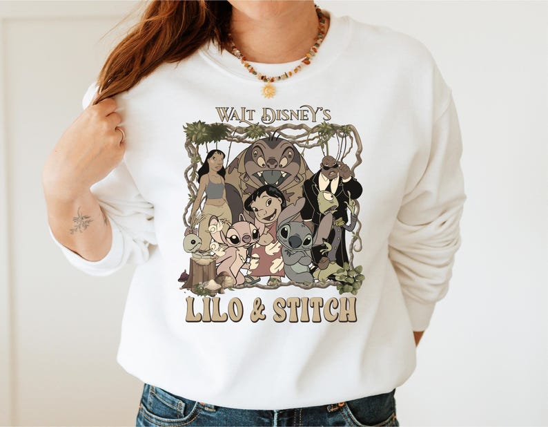 May include: White sweatshirt featuring a graphic of characters from Disney's Lilo & Stitch. The design includes the text "Walt Disney's Lilo & Stitch" in a retro font, with images of Lilo, Stitch, and other characters.