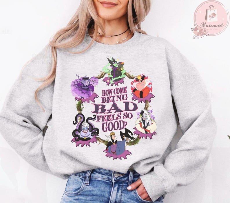 May include: A light gray sweatshirt featuring a colorful graphic of Disney villains. The graphic includes the text "HOW COME BEING BAD FEELS SO GOOD?" in a stylized font, surrounded by images of various villains.