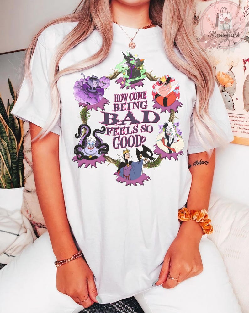 May include: White t-shirt featuring a colorful graphic of Disney villains, including Ursula, the Evil Queen, and Cruella de Vil. The text "HOW COME BEING BAD FEELS SO GOOD?" is printed in the center of the design. The shirt is made of a soft material.