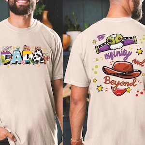Puede incluir: Camiseta beige con la palabra "DADA" en letras coloridas de estilo caricatura en la parte delantera. La parte trasera de la camiseta presenta un gr&aacute;fico con la frase "To Infinity and Beyond" y un sombrero de vaquero.