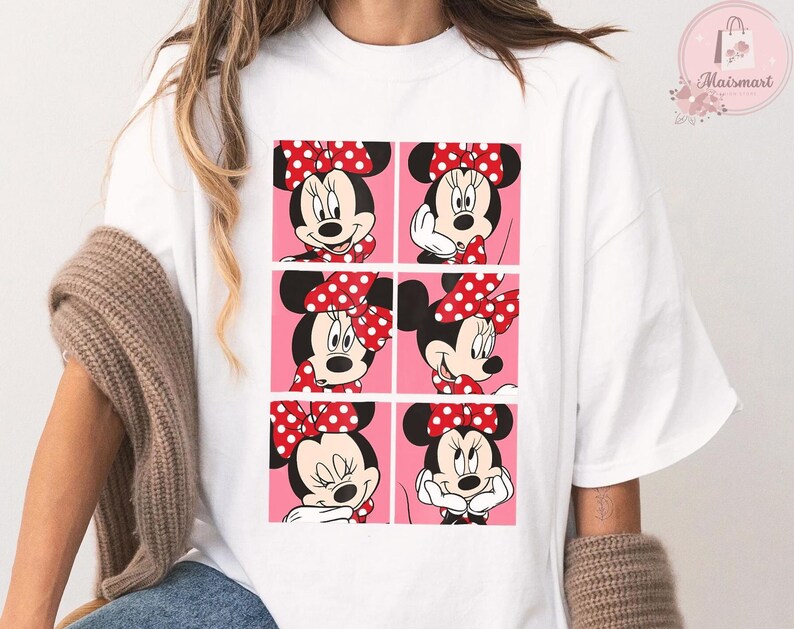 Puede incluir: Camiseta blanca con un dise&ntilde;o de seis paneles de Minnie Mouse en varias poses. Cada panel muestra a Minnie con su lazo rojo de lunares blancos. El fondo es rosa.