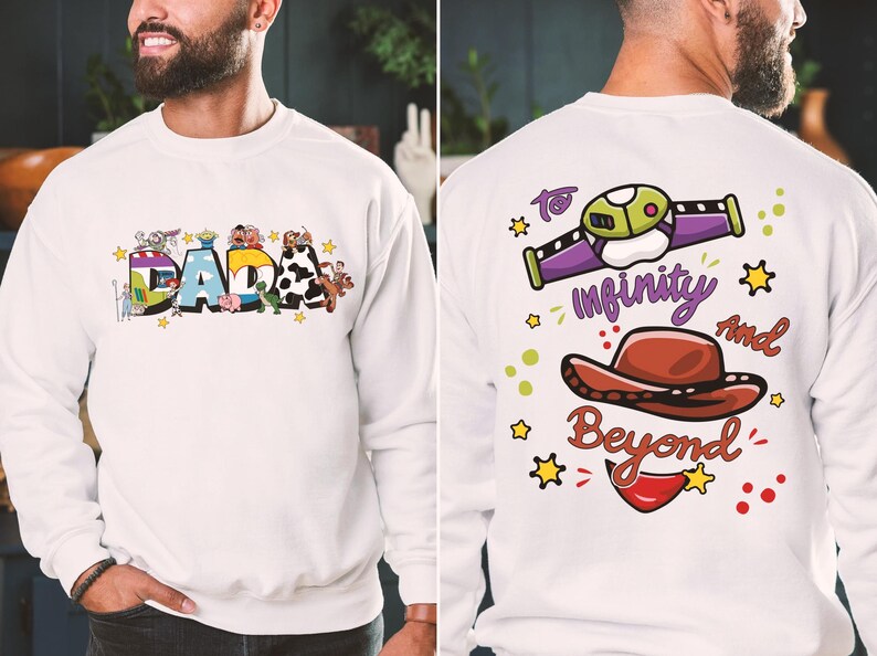 Puede incluir: Sudadera blanca con la palabra "DADA" en letras de bloque coloridas en la parte delantera, decorada con personajes de dibujos animados. La parte trasera presenta una nave espacial, un sombrero de vaquero y la frase "To infinity and beyond."