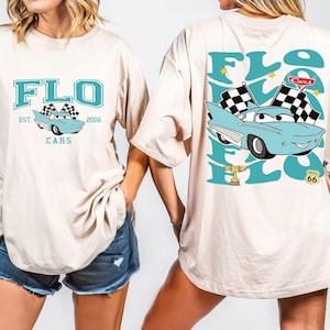 Puede incluir: Camiseta beige con un gr&aacute;fico turquesa de la palabra "FLO" y un coche de dibujos animados con banderas a cuadros. La parte trasera de la camiseta tiene un gr&aacute;fico m&aacute;s grande del coche, las banderas y la palabra "FLO". La camiseta tambi&eacute;n tiene el texto "Cars" y "Est. 2006".