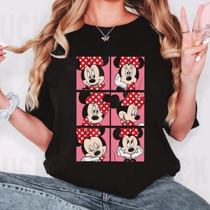 Puede incluir: Camiseta negra con un dise&ntilde;o de cuadr&iacute;cula de caras de Minnie Mouse, cada una con un lazo rojo de lunares sobre un fondo rosa. La camiseta es de cuello redondo.