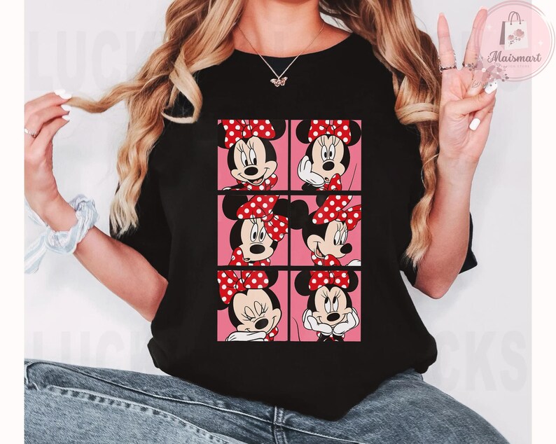 Puede incluir: Camiseta negra con un dise&ntilde;o de cuadr&iacute;cula de caras de Minnie Mouse, cada una con un lazo rojo de lunares sobre un fondo rosa. La camiseta es de cuello redondo.