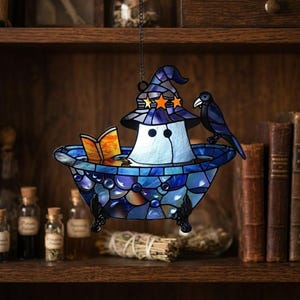 May include: Stained glass Halloween decoration featuring a ghost in a witch hat, reading a book while relaxing in a blue bathtub. A black crow perches on the tub's edge. The decoration hangs from a chain.