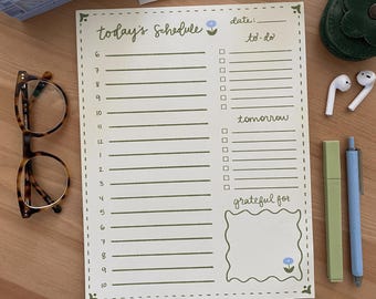 Op de afbeelding: Een gele en groene dagelijkse planner met een to-dolijst, een sectie voor de taken van morgen en een ruimte om dingen op te schrijven waar je dankbaar voor bent. De planner heeft een bloemetjesontwerp in de rechterbovenhoek.