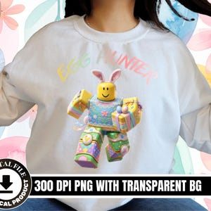 May include: White sweatshirt with the text "EGG HUNTER" in pastel colours. The design features a cartoon character with bunny ears, holding Easter eggs and gifts. The image also includes the text "300 DPI PNG WITH TRANSPARENT BG".