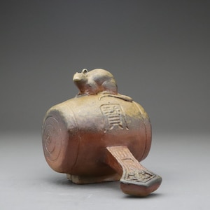 以下が含まれることがあります： 樽型の茶色の陶器彫刻で、上部に小さな動物のフィギュアが付いています。オブジェクトにはハンドルと装飾的なデザインがあります。彫刻には日本語の文字が書かれています。