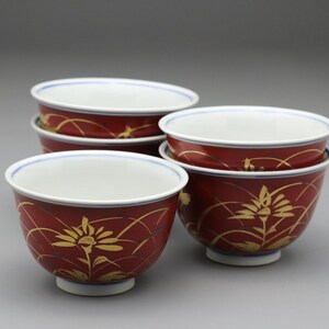 以下が含まれることがあります： 深紅色の陶器のボウル6個セット。ボウルは金色の花の模様と白い内側が特徴です。各ボウルは白いベースと、縁に細い青い線があります。