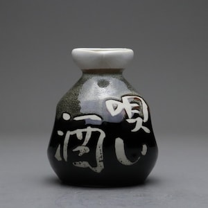 以下が含まれることがあります： 白字の日本語が書かれた、黒い小さな酒瓶。瓶の縁は白く、ボディは濃い緑と黒の斑点模様。日本語の文字は白で、縦書きです。