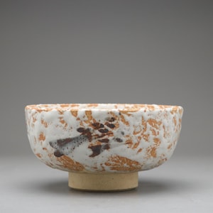 以下が含まれることがあります： 白と茶色の斑点模様の外観とベージュのベースが特徴のセラミックボウル。ボウルは、茶色と黒の抽象的なデザインのテクスチャ表面を持っています。ボウルは、食べ物を提供したり、装飾品として使用される可能性があります。