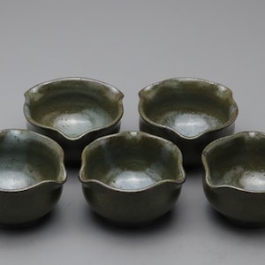 以下が含まれることがあります： 濃い緑色の斑点のある釉薬が施された5つの小さな陶器のボウル。各ボウルは、注ぎ口のある丸みを帯びた波状の縁が特徴です。内面は光沢のある仕上げで、外面はマットな質感になっています。