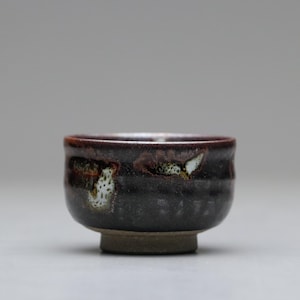 以下が含まれることがあります： 暗い茶色の外観と赤茶色の縁を持つ、手作りの小さなセラミックボウル。 ボウルは、ユニークな白と緑の斑点模様が特徴です。 ボウルの直径は約7.6cm、高さは5cmです。