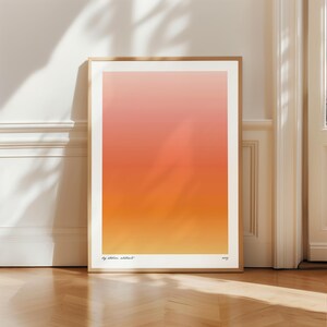 Könnte beinhalten: Ein gerahmter Kunstdruck mit einem Farbverlauf von Pfirsich über Orange nach Gelb. Das Kunstwerk befindet sich in einem Holzrahmen und lehnt an einer weißen Wand. Der Text "by atelier abstract" und das Jahr "2023" sind sichtbar.