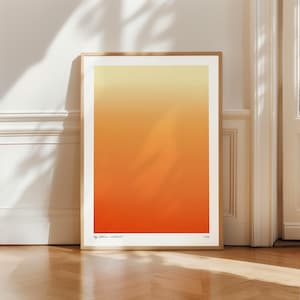 Può includere: Una stampa artistica incorniciata con una sfumatura di colore, che va dal giallo in alto all'arancione in basso. L'opera d'arte è esposta contro un muro bianco e un pavimento in legno. Il testo "by atelier editant" e l'anno "2023" sono in basso.