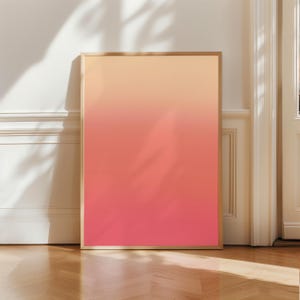 May include: A framed art print featuring a gradient of colors, transitioning from peach at the top to a vibrant coral at the bottom. The artwork is displayed against a white wall and a wooden floor, with shadows from a nearby plant adding depth.