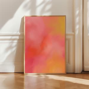 Puede incluir: Una impresión artística enmarcada con una vibrante mezcla de colores. La obra presenta un degradado de tonos rosas, naranjas y amarillos, creando un efecto suave y borroso. El marco de madera añade un toque de calidez a la pieza.